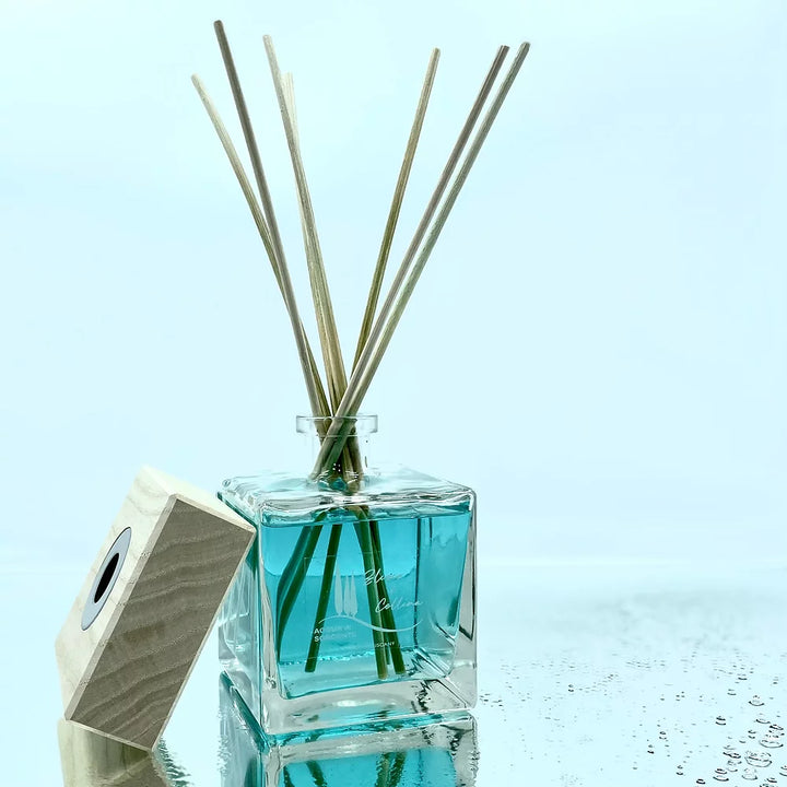 Profumatore d’ambiente Acqua di Sorgente con tappo in legno, liquido azzurro e riflessi d’acqua su sfondo chiaro